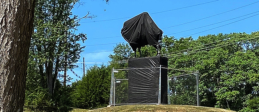 A statue of which two parts are covered in black plastic. It's a covered foundation with exposed horse legs and tail, and a plastic blob on top of it.